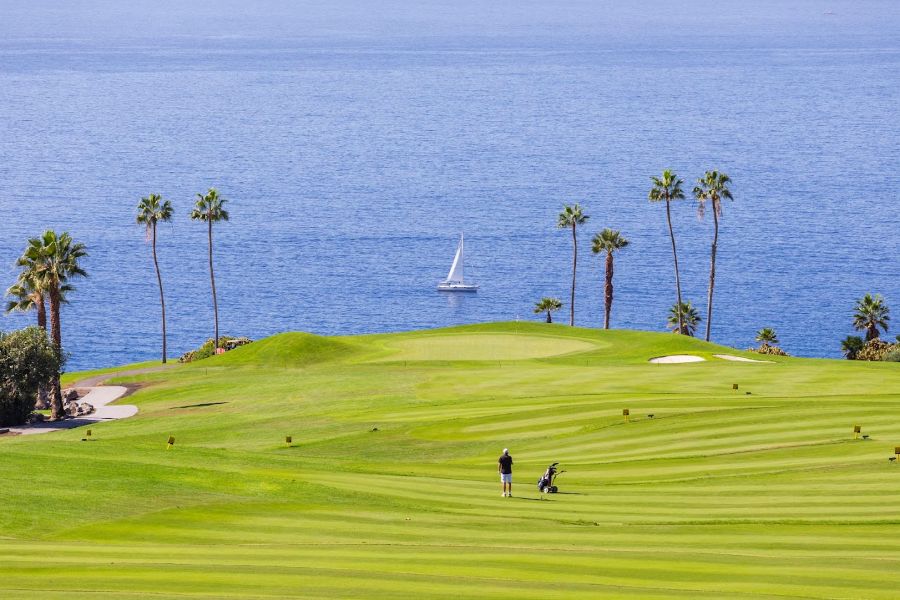 Yacht in the distance as golfers are on cliff top of Costa Adeje golf club