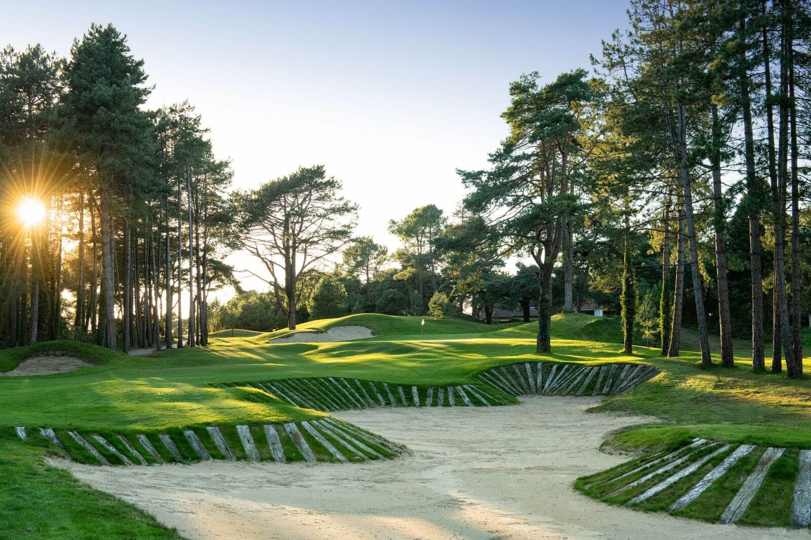 Large bunker protecting the green on Hardelot Les Dunes' third hole with trees surrounding and sun rising
