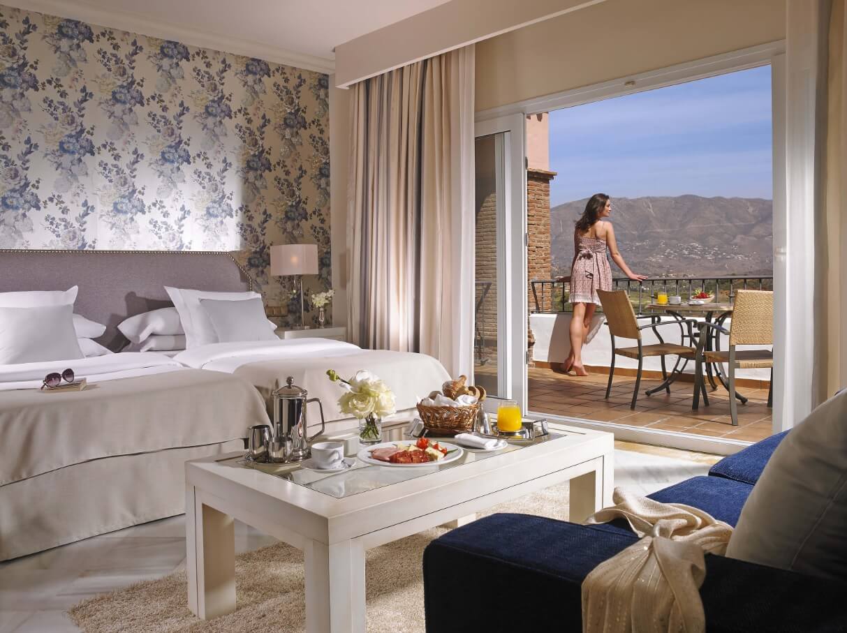 Twin bedroom with table, sofa and open patio doors leading to balcony providing views of the mountains at La Cala Golf Resort