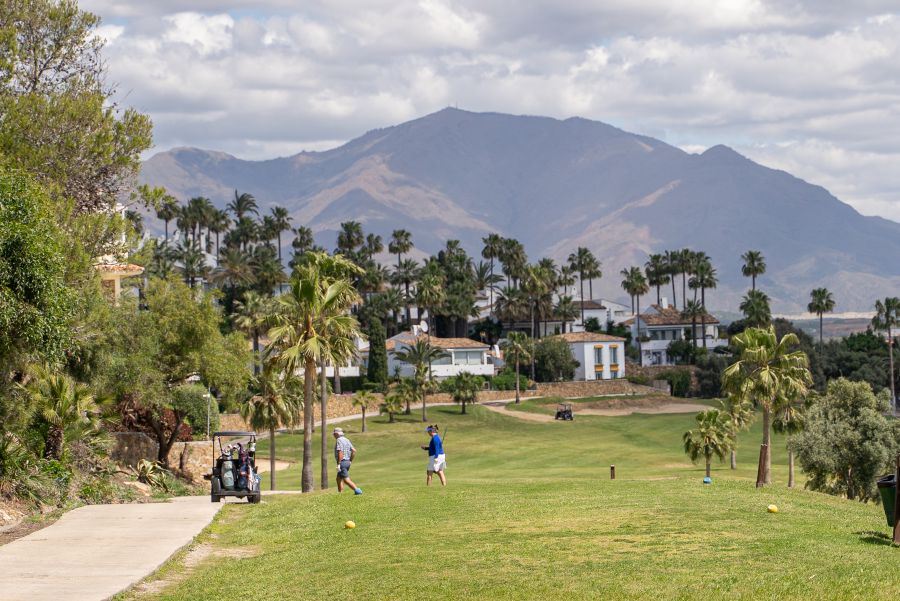 Mountains in the distance at La Duquesa Golf Club with golfers and a buggy on the fairway