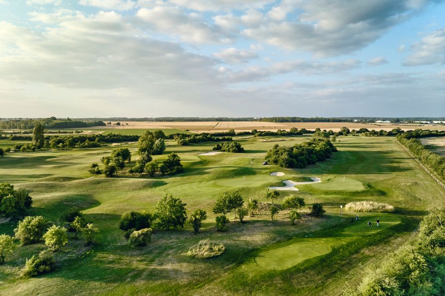 Numerous holes from the air with farming feels in the distance at Le Golf National in France