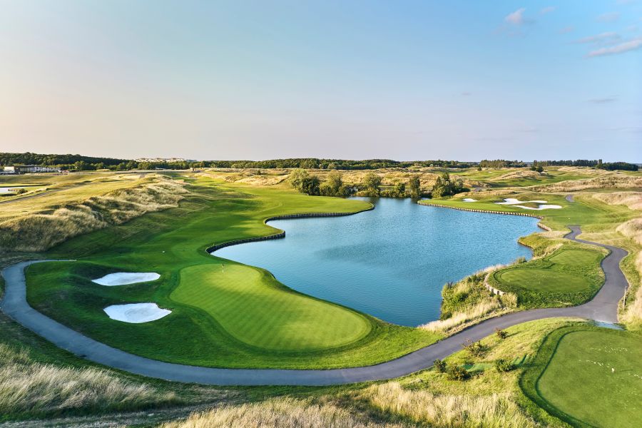 Putting green protected by large blue lake, with buggy path surrounding at Le Golf National in France