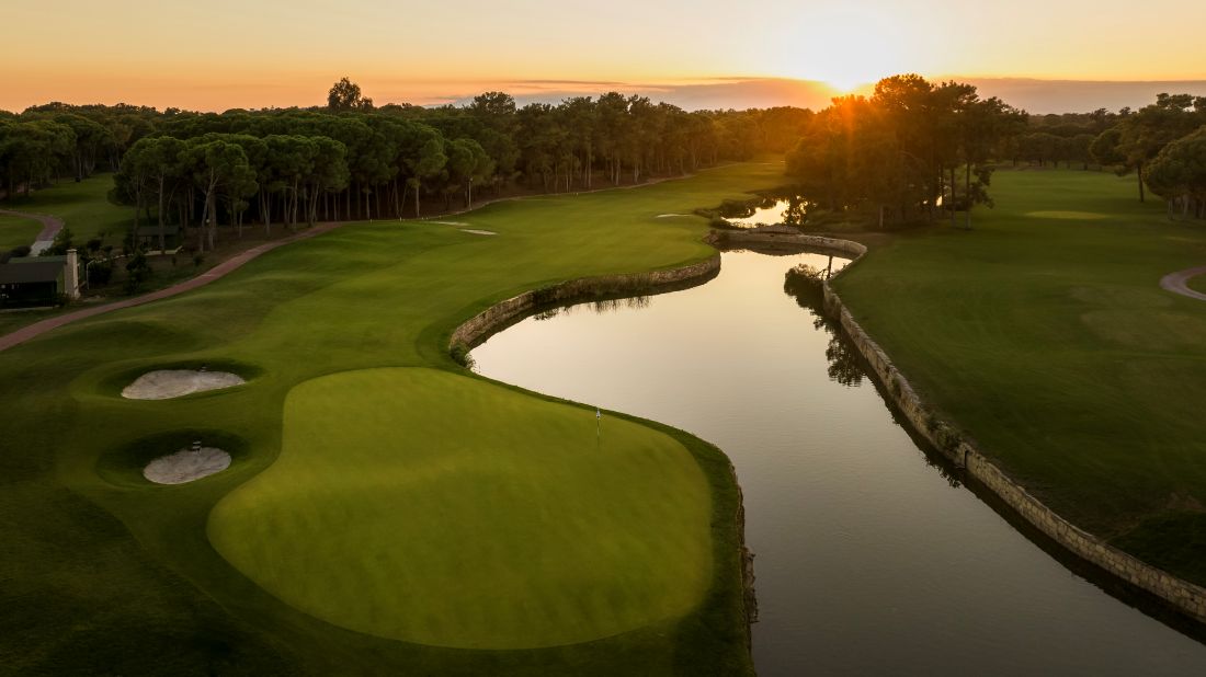 River to the right of the fairway and putting green with sunsetting overhead at National Golf Club in Belek, Antalya