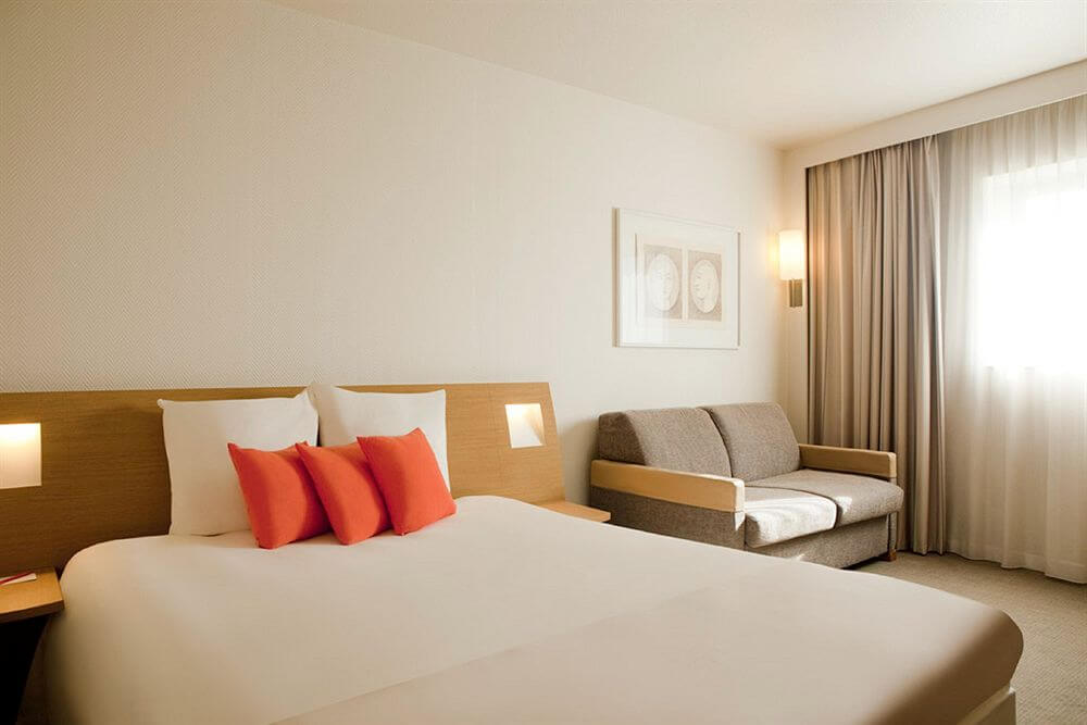 Double bedroom at with sofa and orange cushions on the bed at Novotel Saint Quentin Golf National