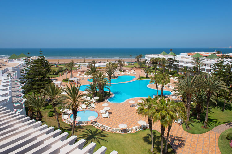 Exterior of Iberostar Founty Beach Hotel Agadir overlooking outdoor swimming pool, blue sea, palm trees and sun loungers