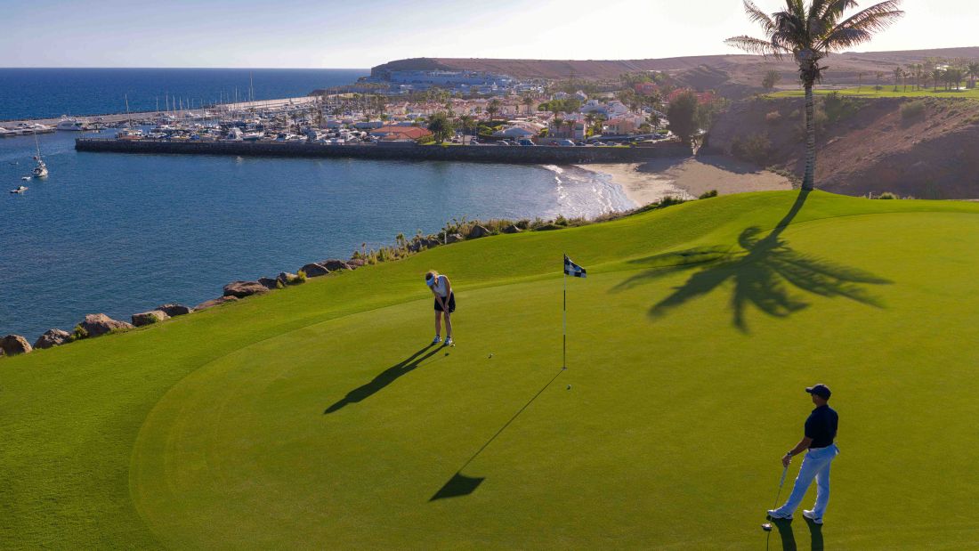 Marina in the background as golfer putts on the green at Lopesan Meloneras