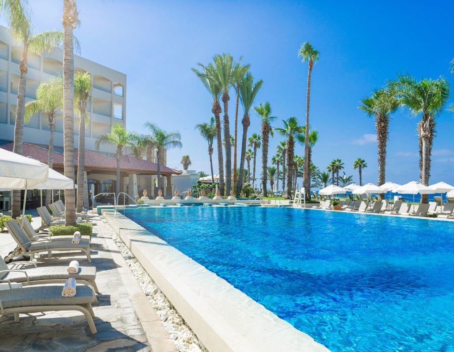 Poolside with sun loungers and palm trees at Alexander The Great Beach Hotel
