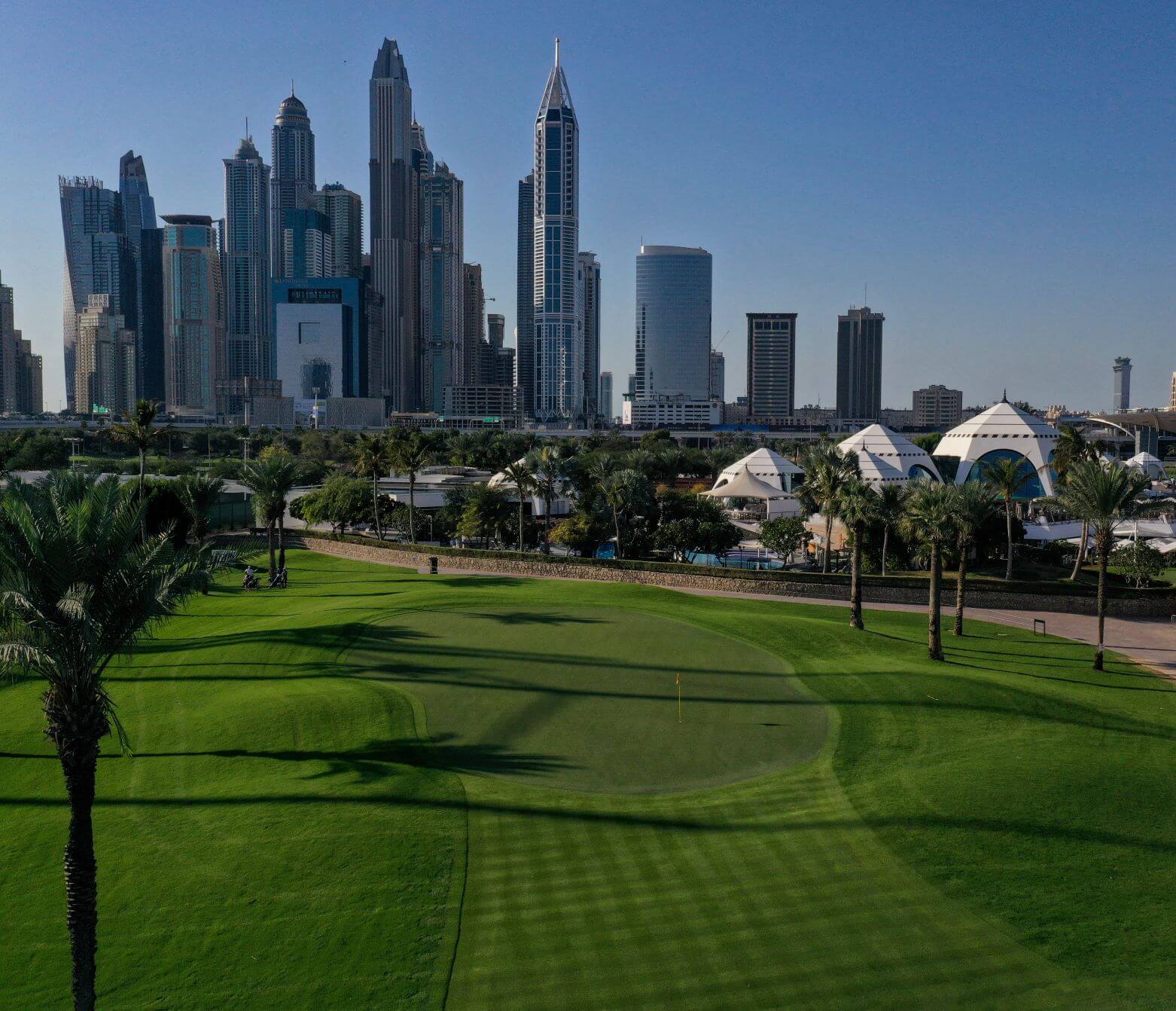 Blue skies and green fairway with clubhouse in the distance overlooked by skyline at Majilis Golf Course at Emirates Golf Club