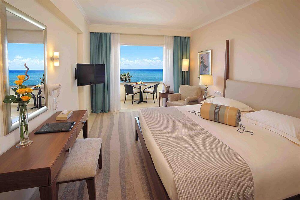 Double bedroom at Alexander The Great Beach Hotel with television mounted on the wall and patio to balcony with sea view