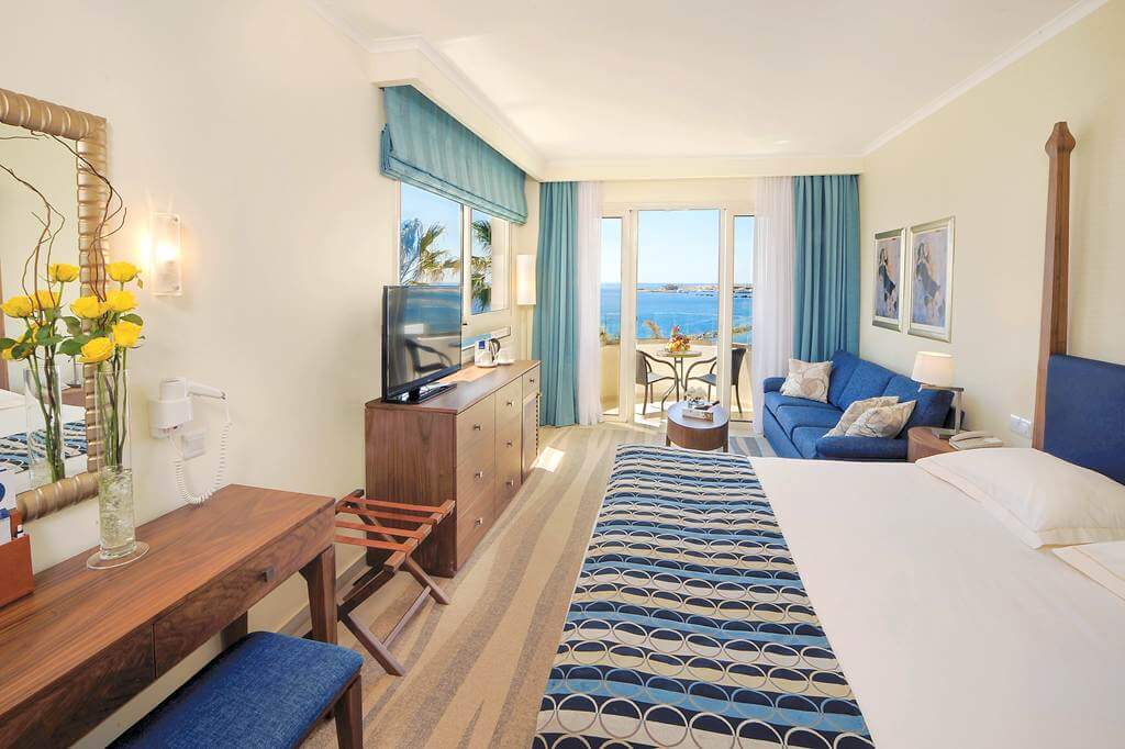 Double bedroom at Alexander The Great Beach Hotel with television, sofa and patio doors leading to private balcony