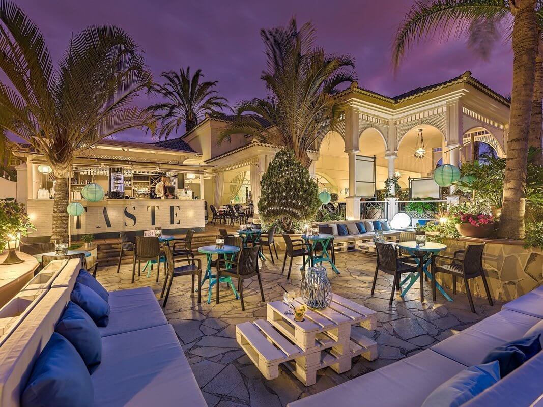 Courtyard of bar at Gran Oasis Resort in the evening with sofa, chairs, and wooden pallet table