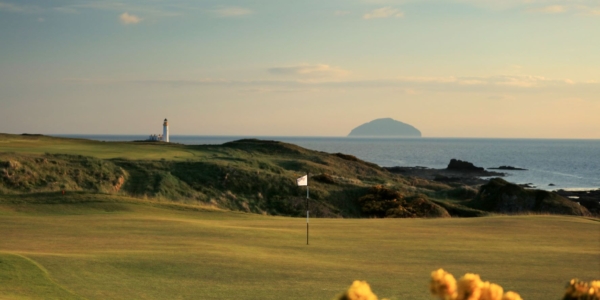 Lighthouse in the distance and flag on the green on the golf course at Trump Turnberry Golf Resort
