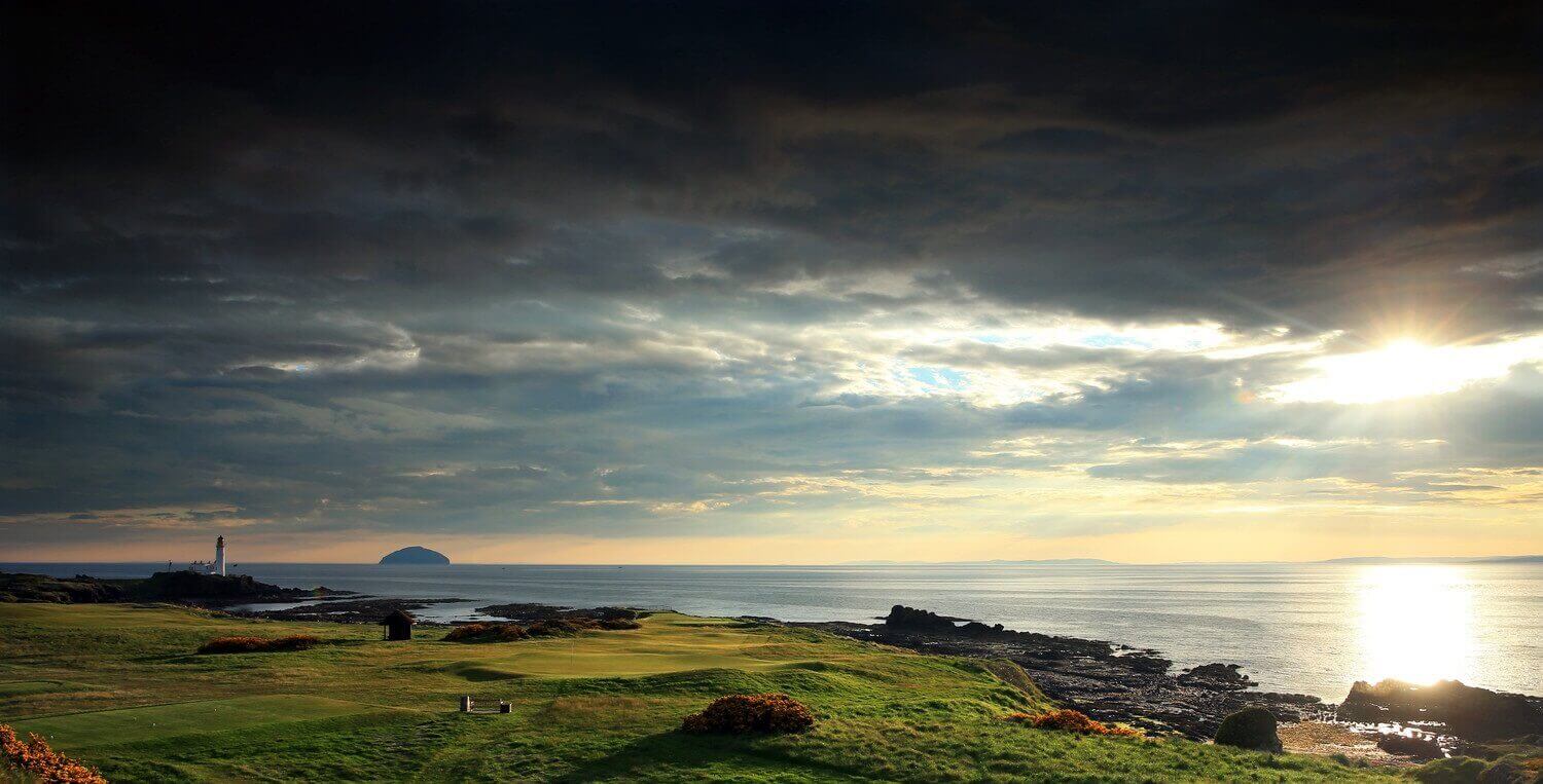 Golf course with lighthouse and sea in the distance at Trump Turnberry Resort in Scotland