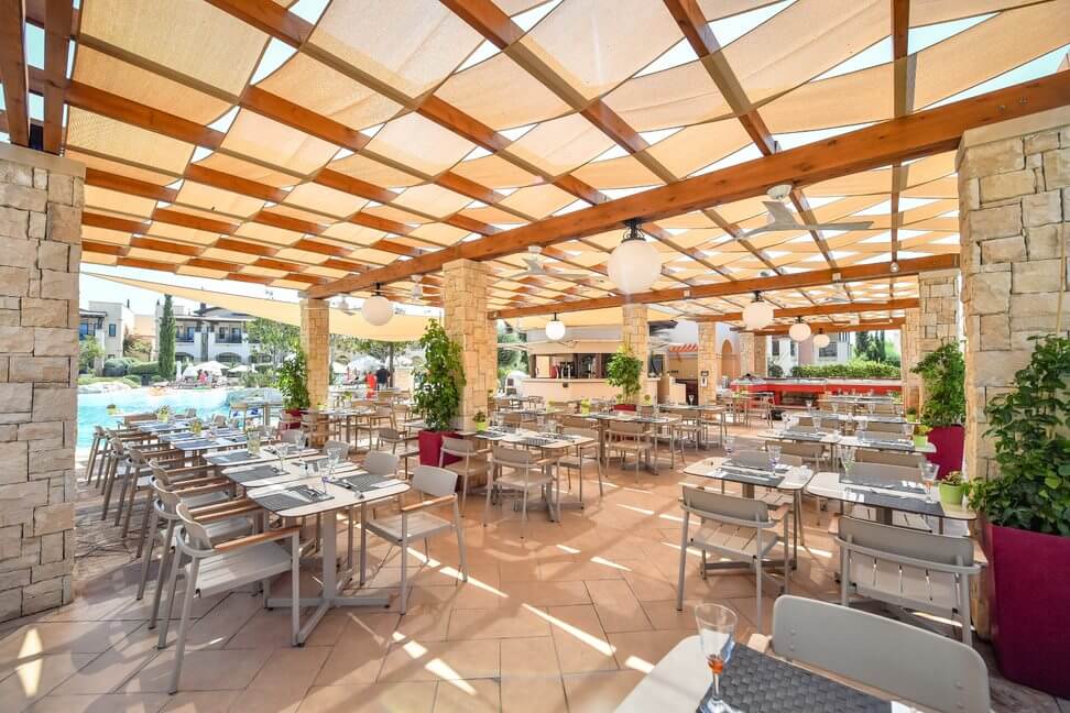 Restaurant with tables set by the outdoor swimming pool at Aphrodite Hills Resort