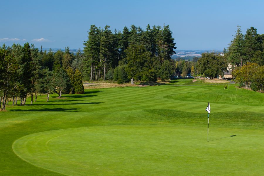 White flag on putting green with blue sky and green trees in the distance at Slaley Hall Hotel, Spa And Golf Resort
