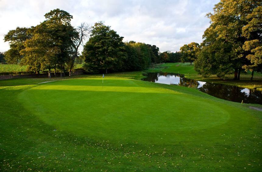 Green with flag in the hole which is protected by a lake at Mottram Hall
