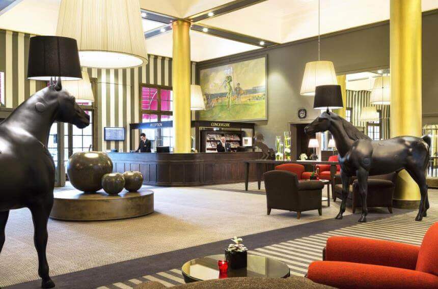 Reception desk and lobby area at Hotel Barriere L'Hotel du Golf Deauville with red chairs and horse sculptures