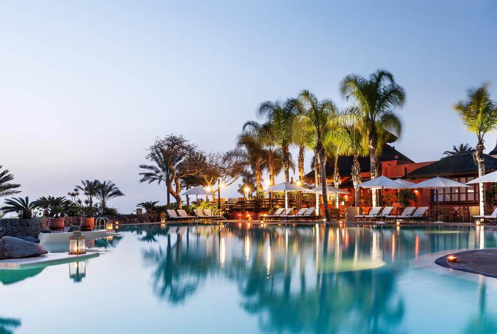 Swimming pool at The Ritz-Carlton Abama Resort in the evening with candlelit lighting, sun loungers and palm trees