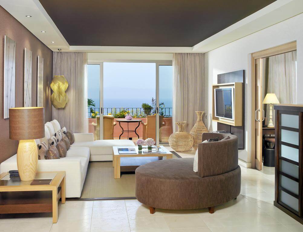 The Ritz-Carlton Abama Resort living area with cream sofa, brown chair, television and private balcony with wicker chairs