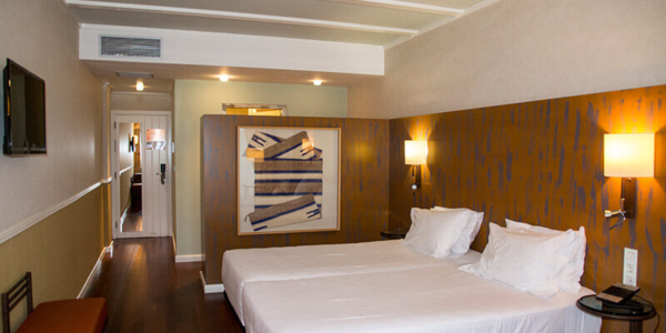 Twin beds in bedroom at Hotel Nuevo Portil Golf with television mounted on wall and art on display