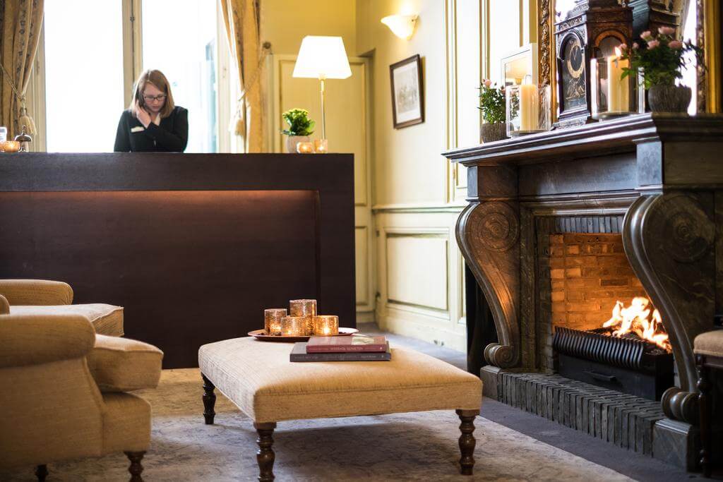 Reception desk at Martin's Relais with open fire, logs burning, chair, foot stool, candles and books resting on foot stool, receptionist on telephone