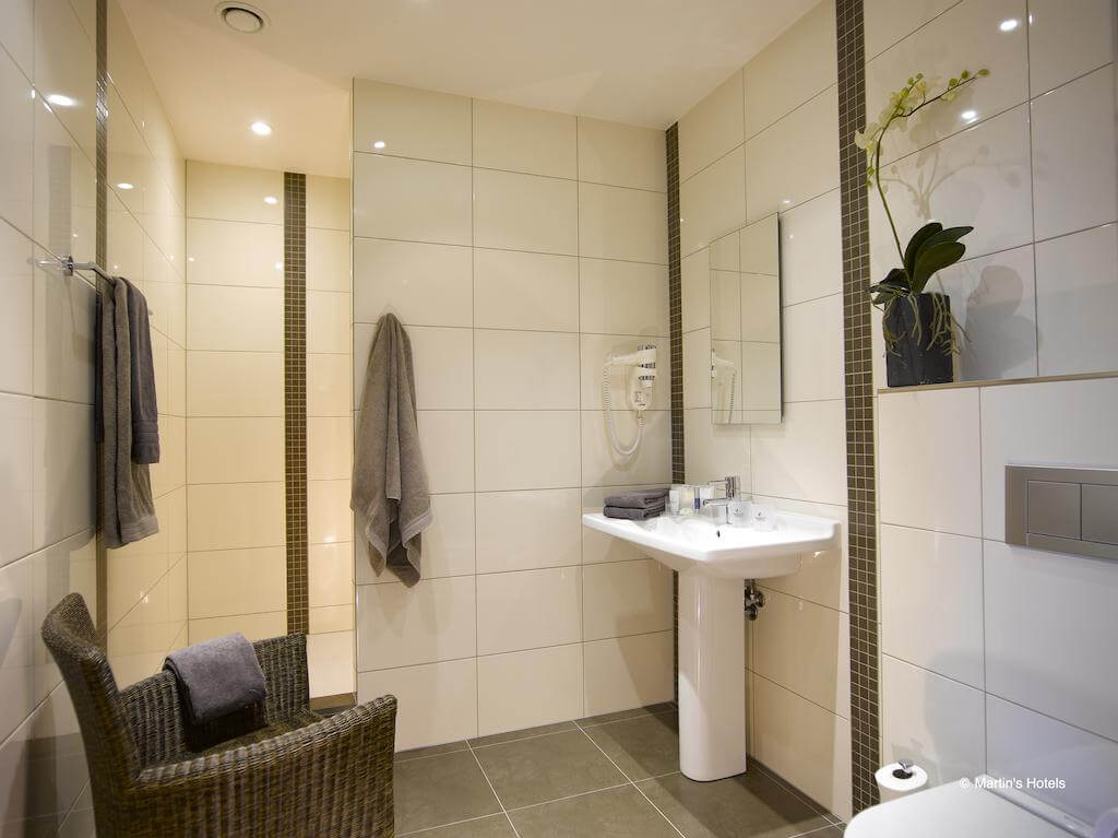 Tiled bathroom with wicker chair at Martin's Waterloo, with separate shower cubicle, hairdryer, toilet and sink
