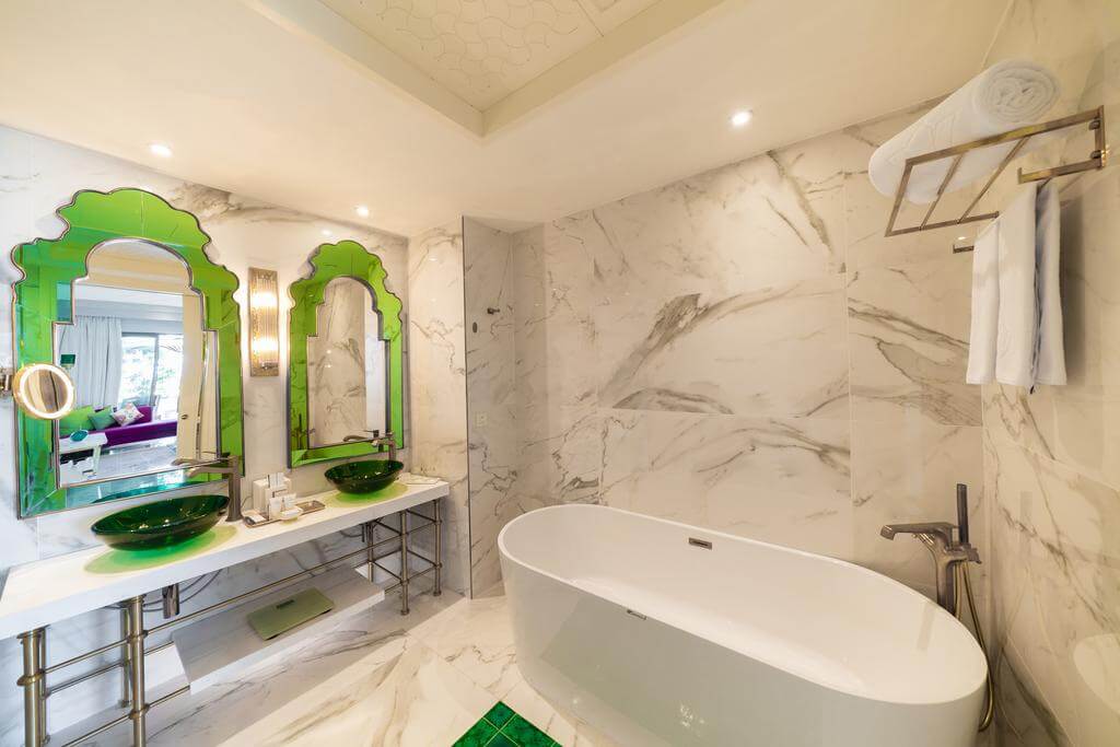Rixos Premium Saadiyat Island bathroom with green framed mirror, marble tiles, bath tub and twin sinks