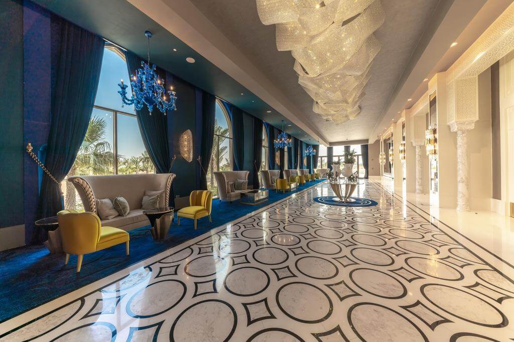 Lobby area at Rixos Saadiyat Island with marble floor, green curtains, yellow seats, grey sofas and blue chandeliers