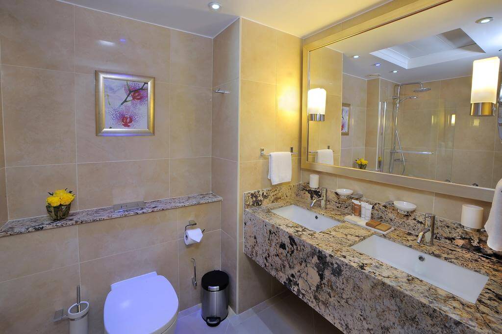 Bathroom at Olympic Lagoon Resort Paphos with two sinks, toilet, mirror and toiletries