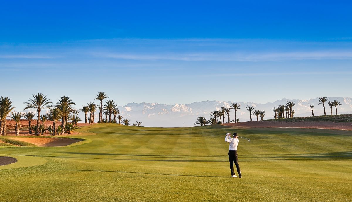 Golfer on the fairway at Assoufid with trees and blue sky in the background