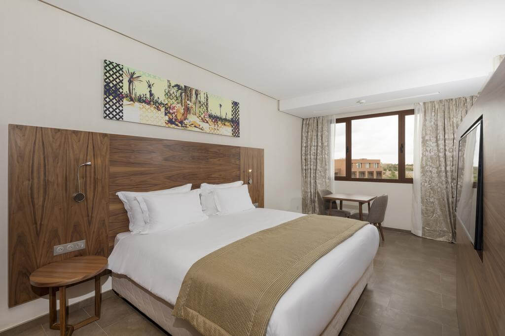 Be Live Experience Marrakech Palmeraie's double bedroom with bedside table, throw on bed, flat screen television, table and two chairs