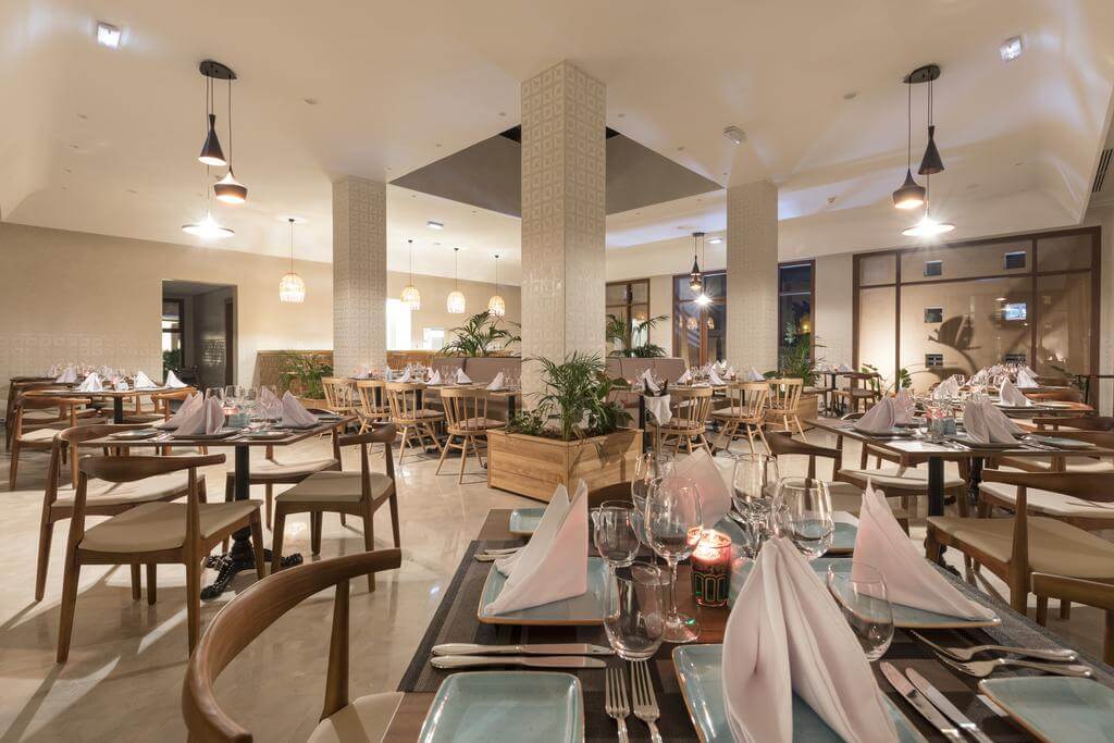 Tables set in restaurant at Be Live Experience Marrakech Palmeraie with lights hanging from ceiling and plants decorating the room
