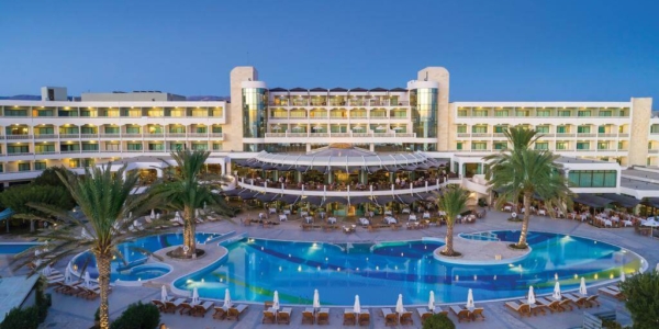 Exterior of Constantinou Bros Athena Beach Hotel overlooking the swimming pool, sun loungers and palm trees in the evening