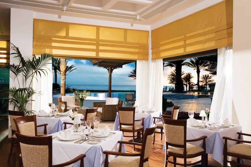 Restaurant at Constantinou Bros Athena Beach Hotel with tables set and views of the swimming pool and sea