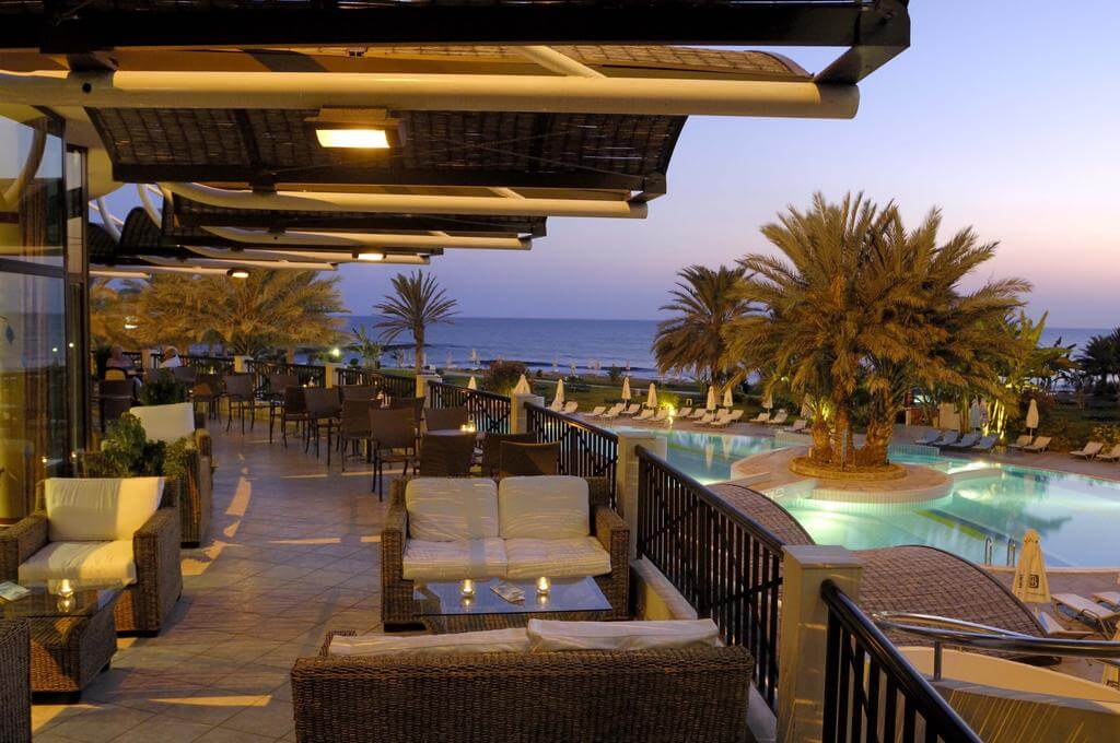Bar at Constantinou Bros Athena Beach Hotel with seating on candlelit balcony overlooking the swimming pool in the evening
