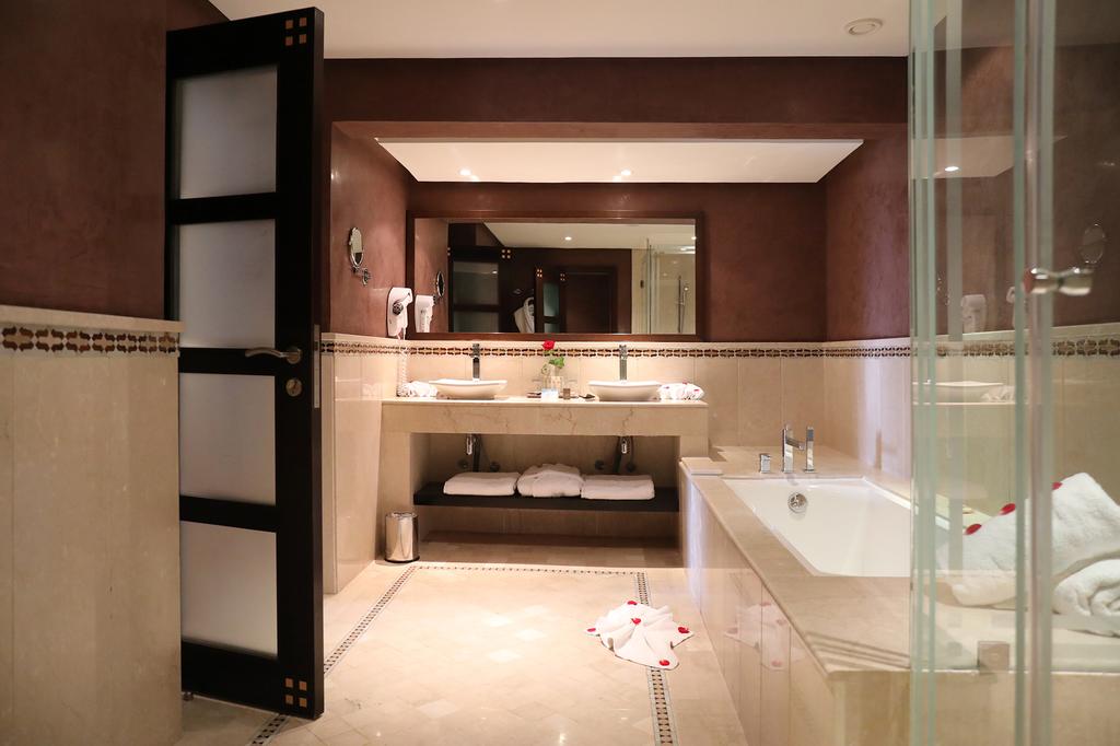 Bathroom at Kenzi Menara Palace And Resort with two sinks, bath tub, shower cubicle and towels