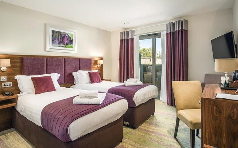 Twin bedroom with fresh towels, desk and mounted television at Cotswolds Hotel Spa And Golf