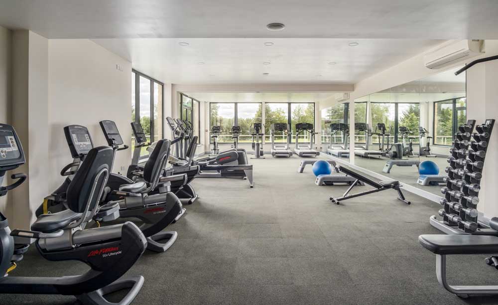Gym with free weights, cardio machines and walled mirrors at Cotswolds Hotel Spa And Golf