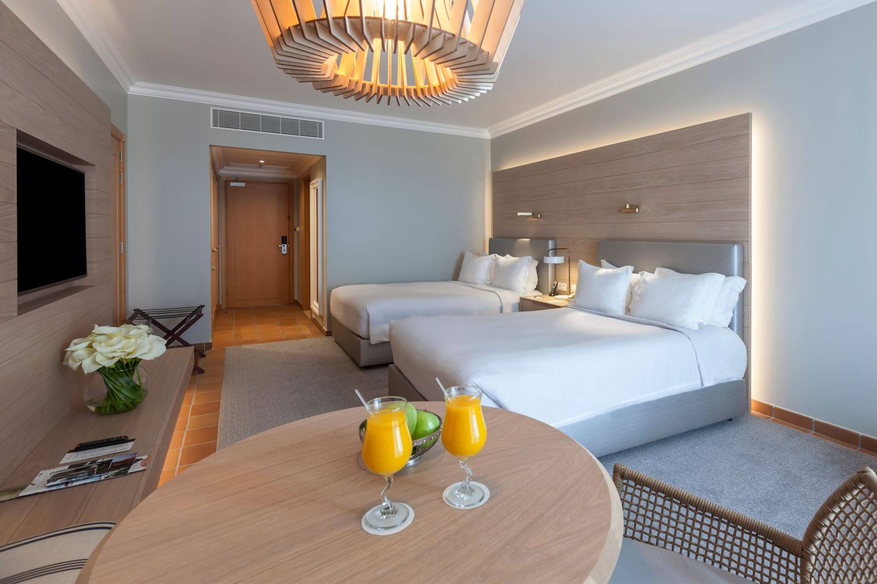 Twin bedroom at Marriott Praia D'El Rey Resort with television on wall, table with two glasses of orange juice on