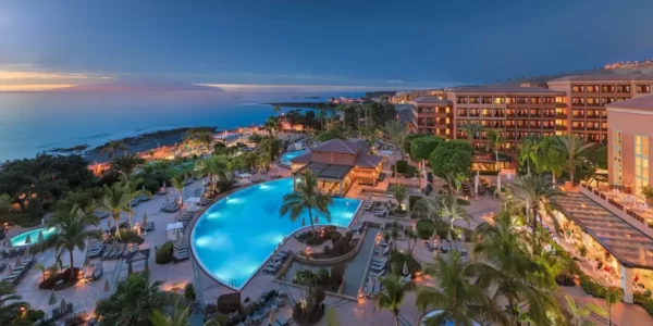 H10 Costa Adeje Palace at night with swimming pool, palm trees and the sea
