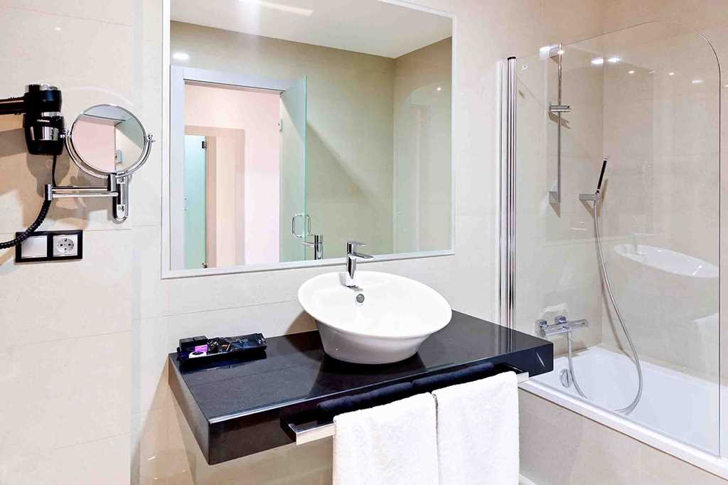 Bathroom at DNA Monse Hotel Spa And Golf with mirror on wall, sink, shower over bathtub and clean towels