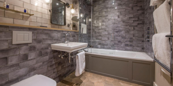 Bathroom at Sandburn Hall with toilet, sink, bath tub and shower. Grey metro tiles decorate it.