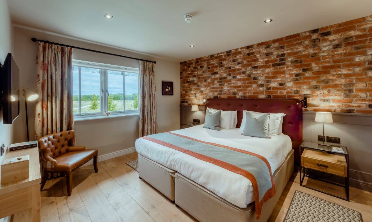 Bedroom at Sandburn Hall with double bed, exposed brick effect wall, and window overlooking the golf course
