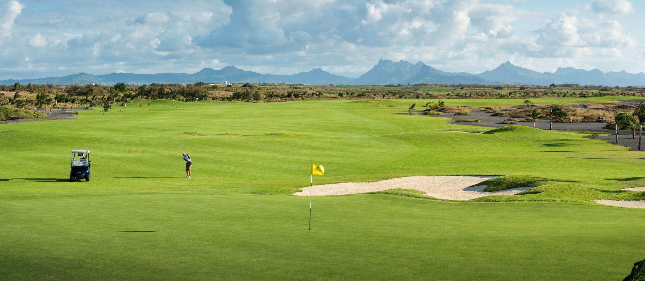 Lush green fairway at Mont Choisy Le Golf with female golfer and buggy playing to yellow pin