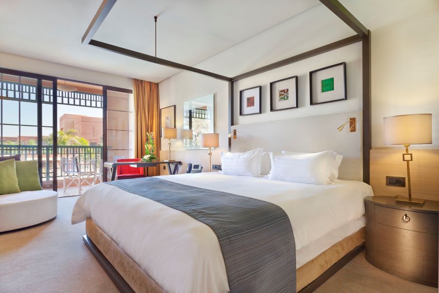 King bed with pictures on wall and sliding door leading to balcony at Pickalbatros Hotel Du Golf Palmeraie Marrakech