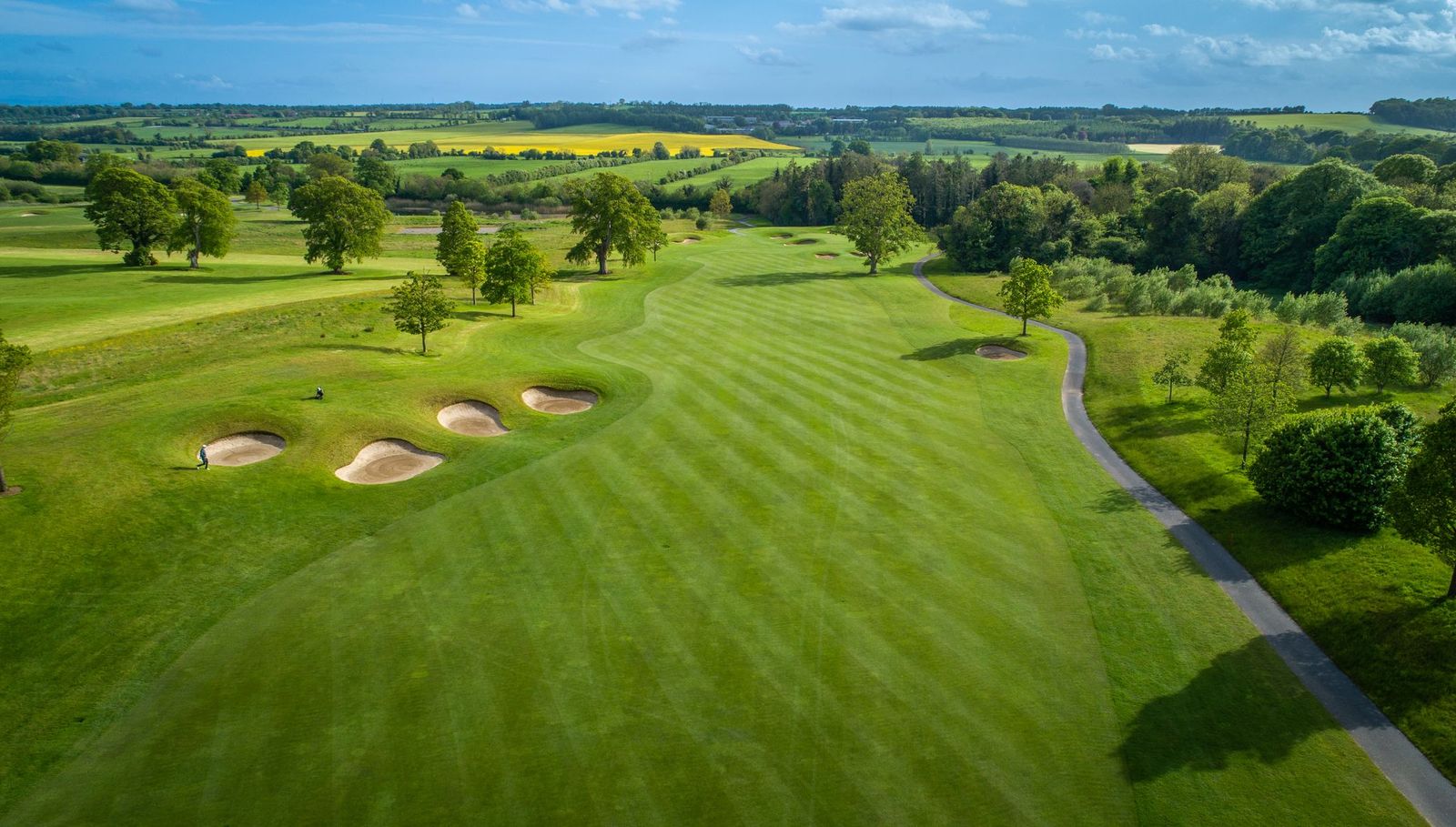 Green fairway with three bunkers to the left and blue sky overhead